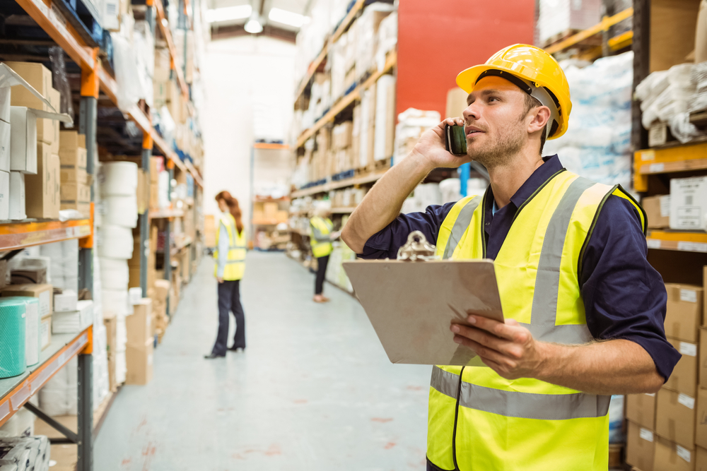 Warehouse worker talking on the phone holding clipboard in a large warehouse Warehouse worker talking on the phone holding clipboard in a large warehouse